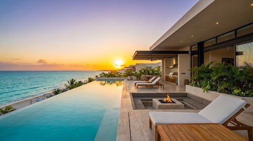 An expansive, opulent beachfront penthouse terrace in Playacar Phase I. The view overlooks pristine white sand and brilliant turquoise Caribbean waters. The terrace features luxurious modern outdoor furnishings, a private plunge pool, and glass railings that offer uninterrupted ocean views under a clear, sunny sky.
